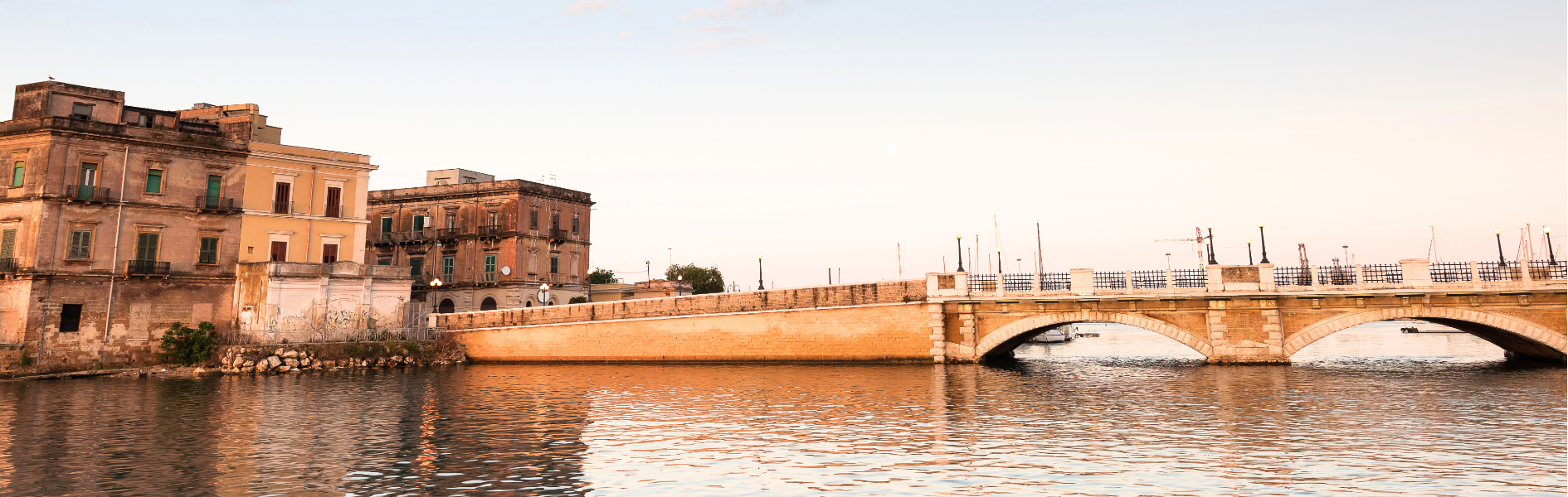 Ponte storico, edifici antichi e acqua calma in un paesaggio sereno.