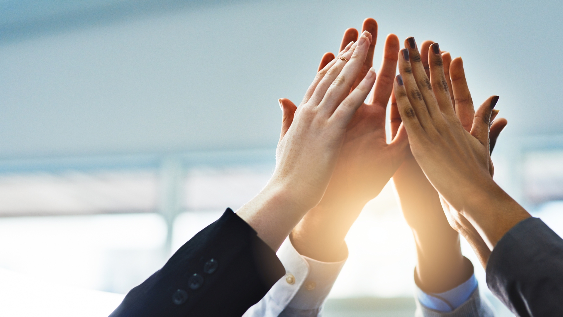 Mani di diverse persone che si uniscono in segno di collaborazione in un ambiente di lavoro luminoso.